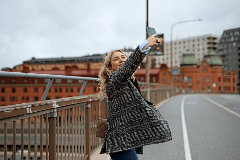 Kvinna ler och tar en selfie på sig själv med sin mobil utomhus.